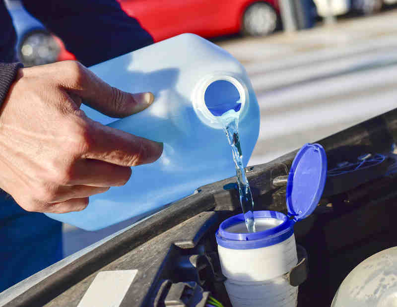 hand filling washer liquid in car's reservoir
